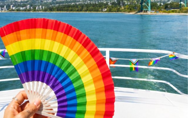 rainbow colored hand fan being held in the first plane with the water on the background.